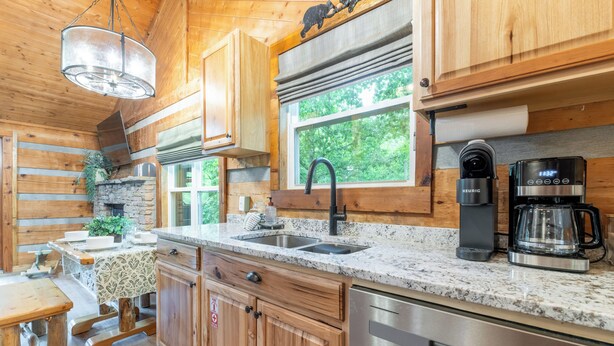 A kitchen with wooden cabinets, granite countertops, a stainless steel dishwasher, a coffee maker, and a window with a view of greenery. - Visit Dollywood! 2 King Beds! Cedar Brooke Haven (Sevierville)