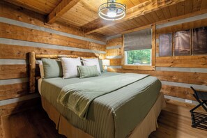Ein Schlafzimmer einer Holzhütte mit einem Bett, Kissen, einem Fenster und einer Deckenleuchte.