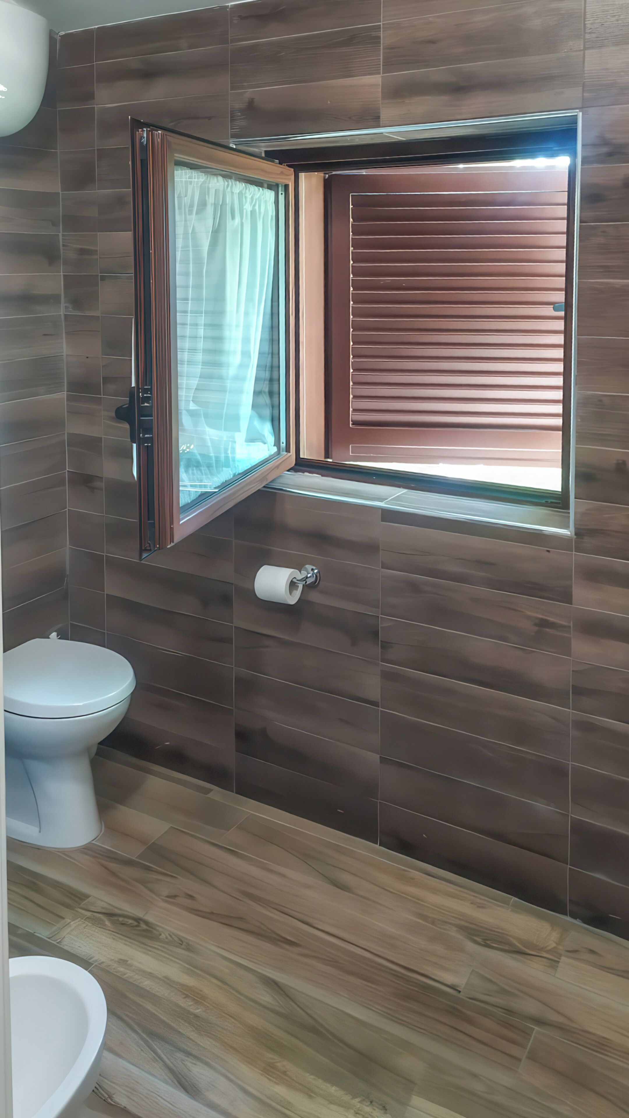 Un bagno con il water, una finestra con tenda e un portascopino.