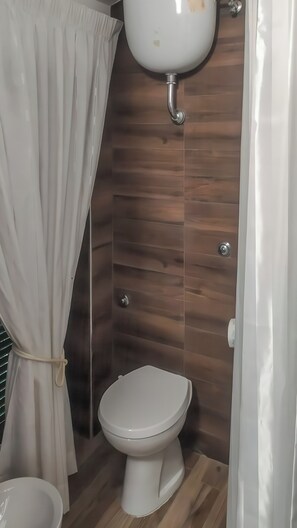 Een badkamer met toilet, douchegordijn en houten wandpanelen.