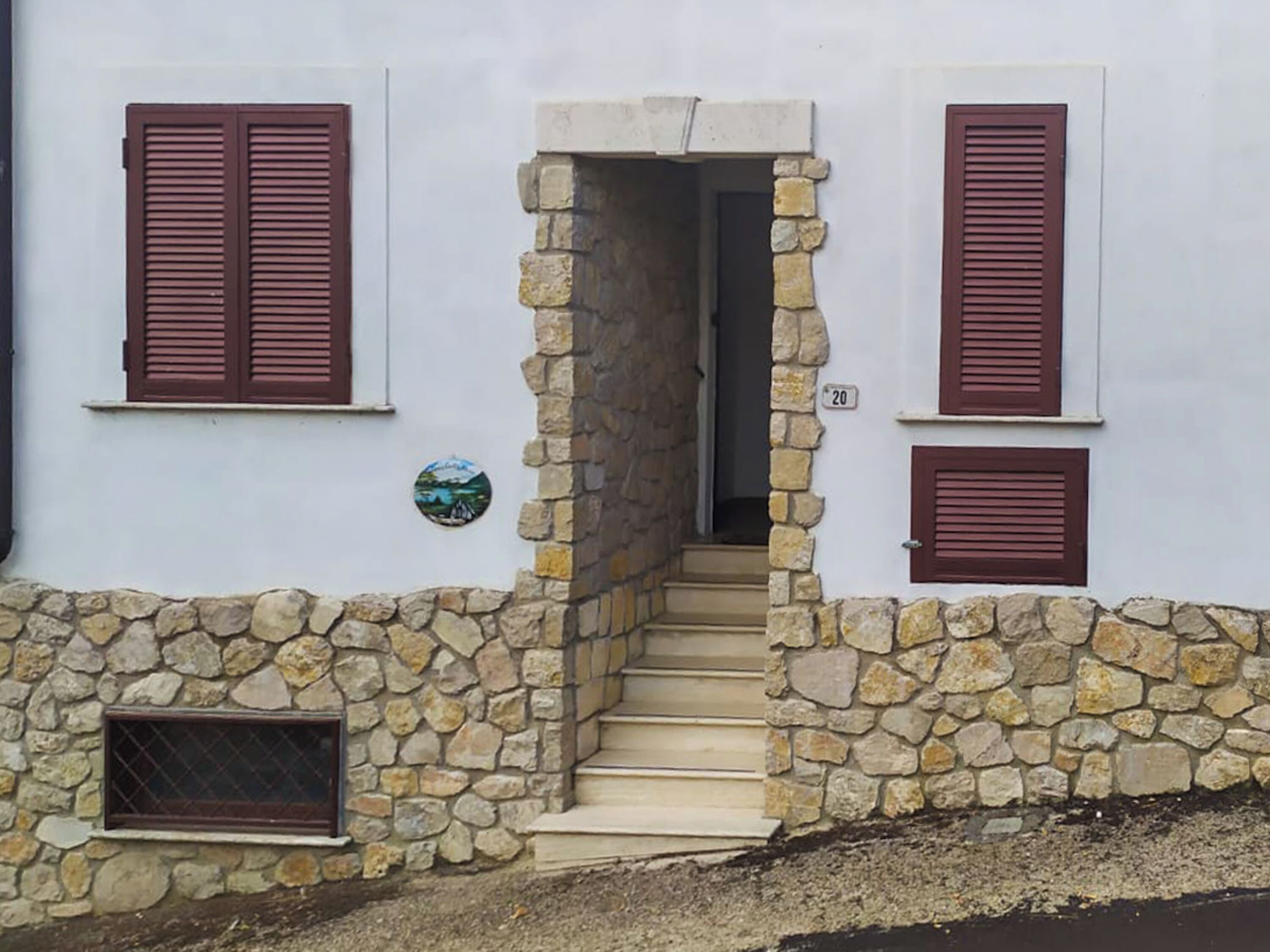 Un edificio de paredes de piedra, con una escalera que lleva a una puerta y dos ventanas con contraventanas.
