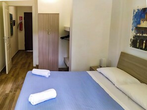 Een hotelkamer met een bed, een kledingkast, een nachtkastje en een schilderij aan de muur.