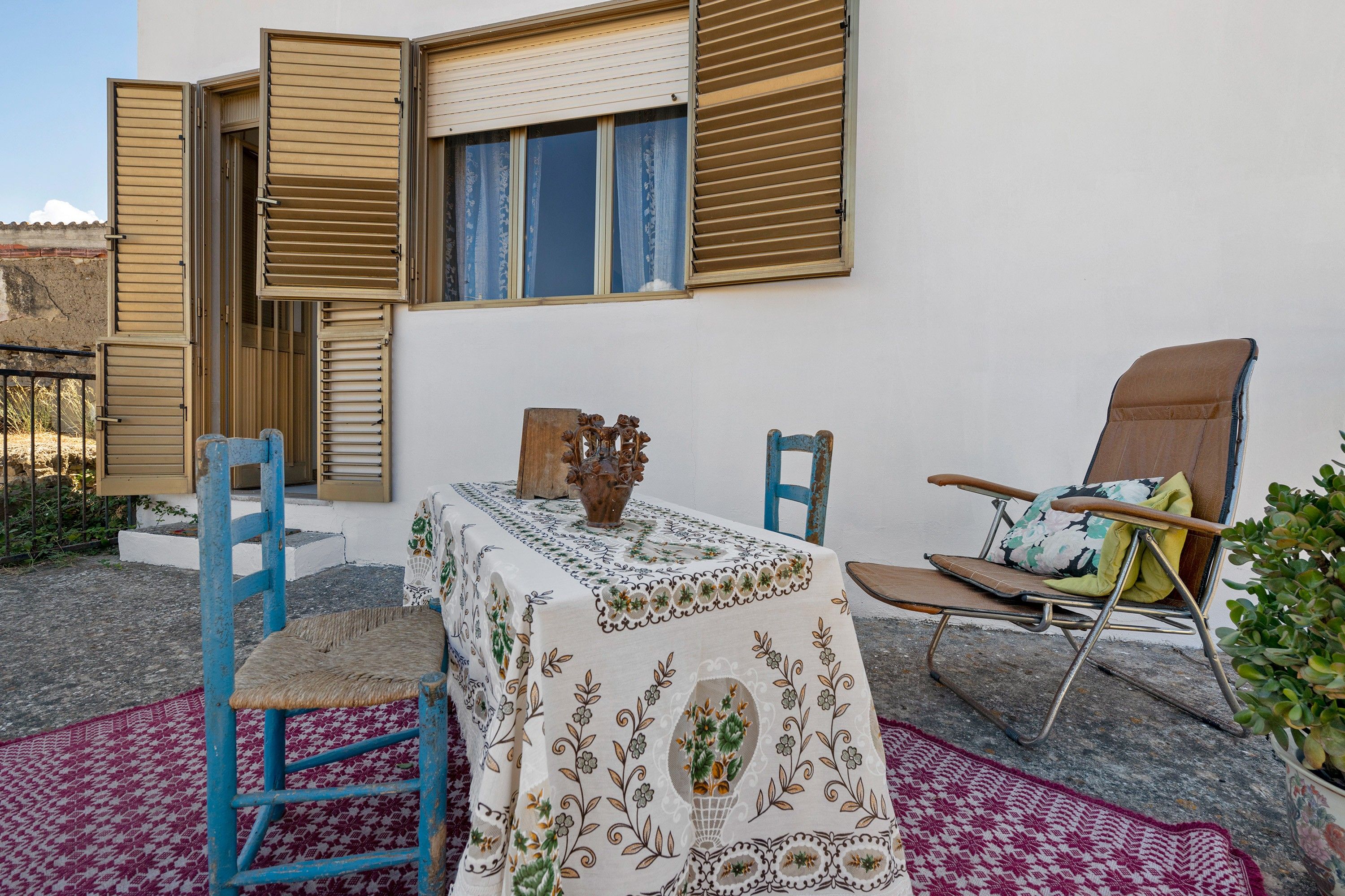 A room with a table set with a tablecloth, chairs, and a potted plant.