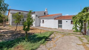A residential building with a red-tiled roof, a small garden area with grass and a few trees, and a clear blue sky.