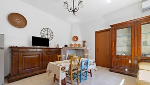 A dining area with a table set for four, wooden cabinets, a television, wall clocks, and a chandelier.