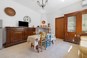 A dining area with a table set for four, wooden cabinets, a television, wall clocks, and a chandelier.
