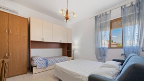 A bedroom with a bed, a chair, a wardrobe, and a window with curtains.