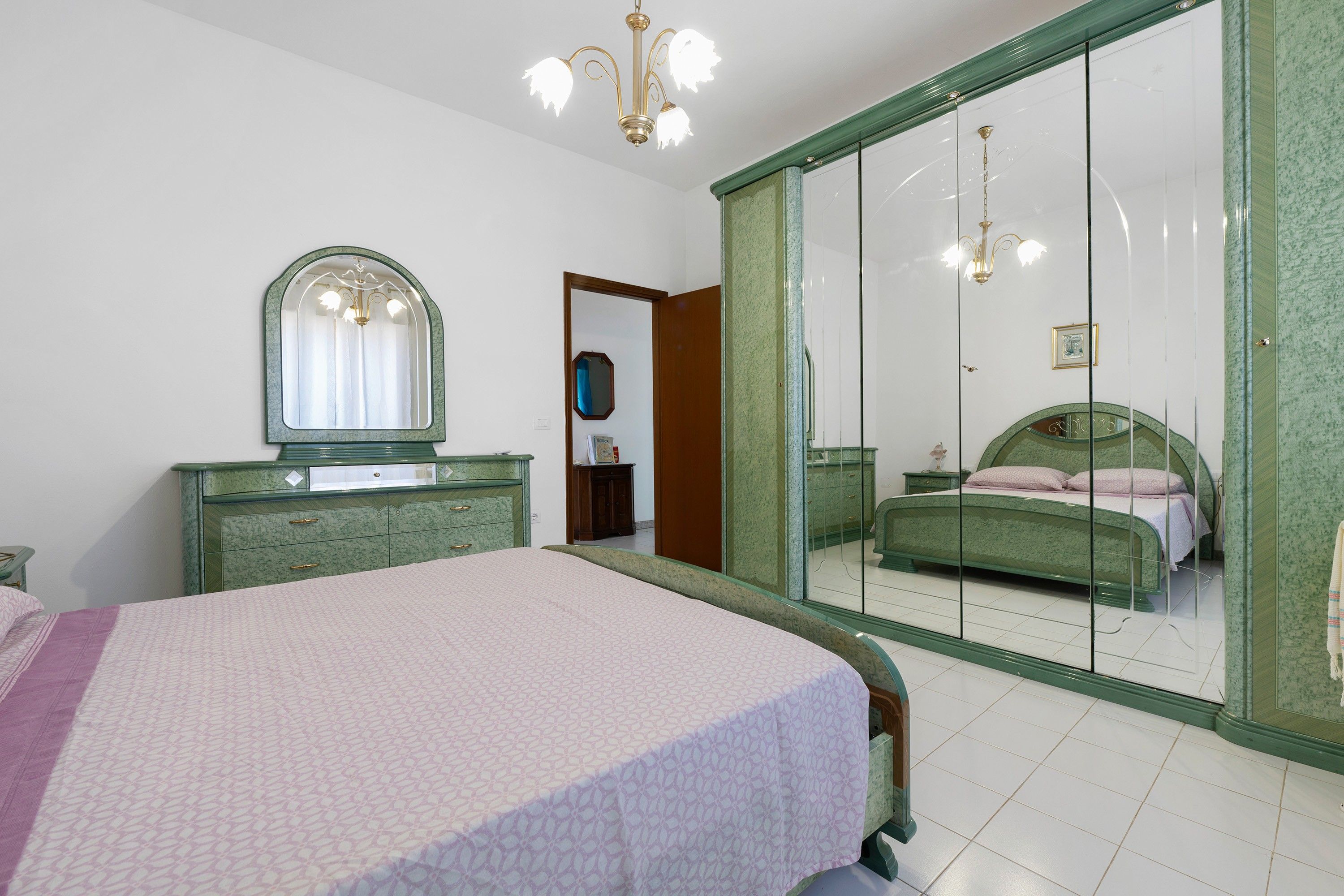 Ein Schlafzimmer mit Bett, Kommode, Spiegel und Kleiderschrank mit Ganzkörperspiegel.