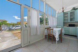 Ein Zimmer mit Esstisch, Stühlen, einer Küchenzeile mit Schränken und einer Glasschiebetür zu einem Außenbereich.