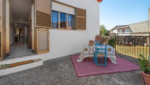 A residential building with a patio area featuring a table and chairs, a potted plant, and a stone wall.