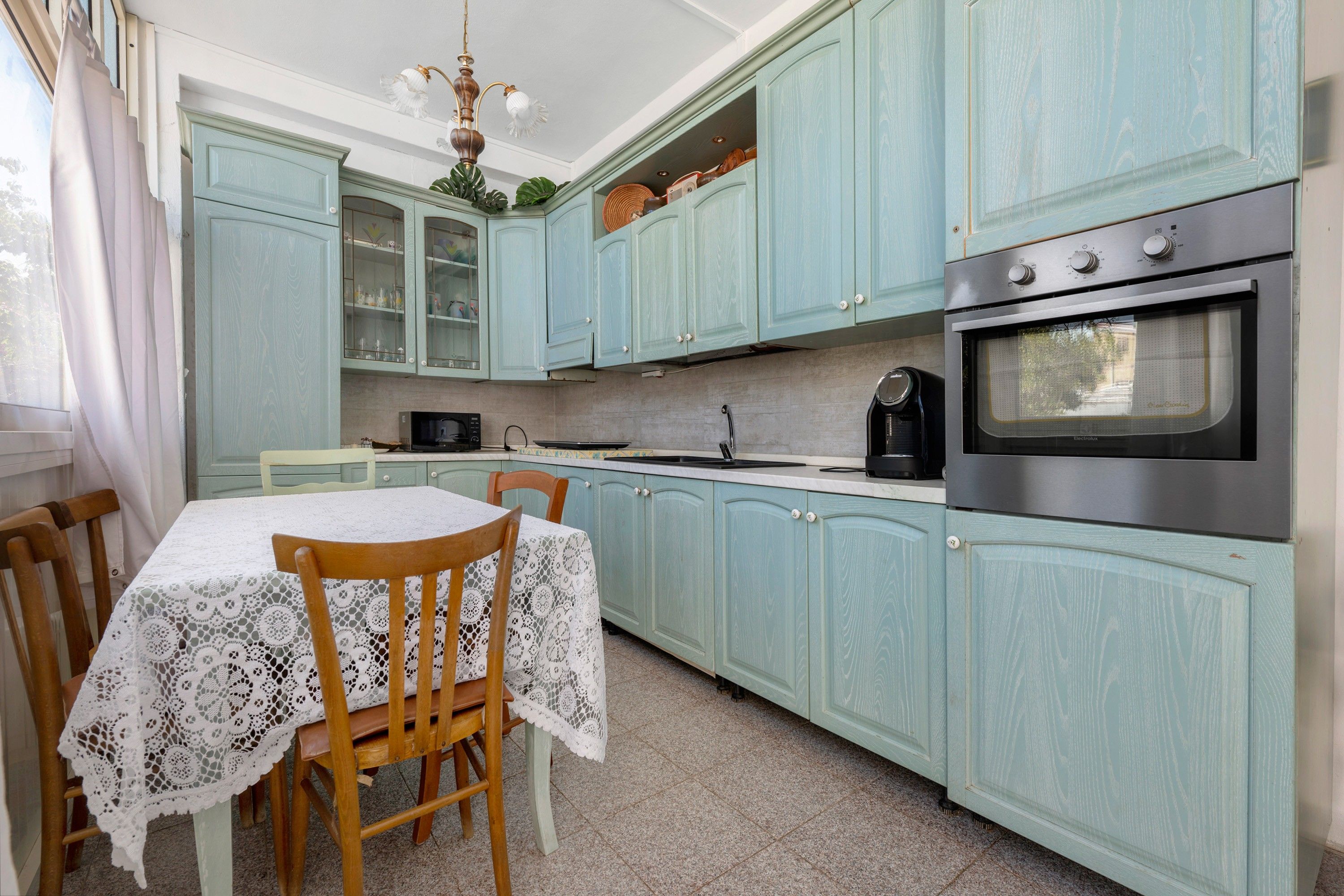 A kitchen with teal cabinets, a dining table with lace tablecloths, and a stove.
