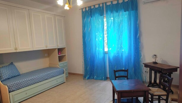 Een kamer met een bed, een tafel en een stoel. Er is een raam met blauwe gordijnen.