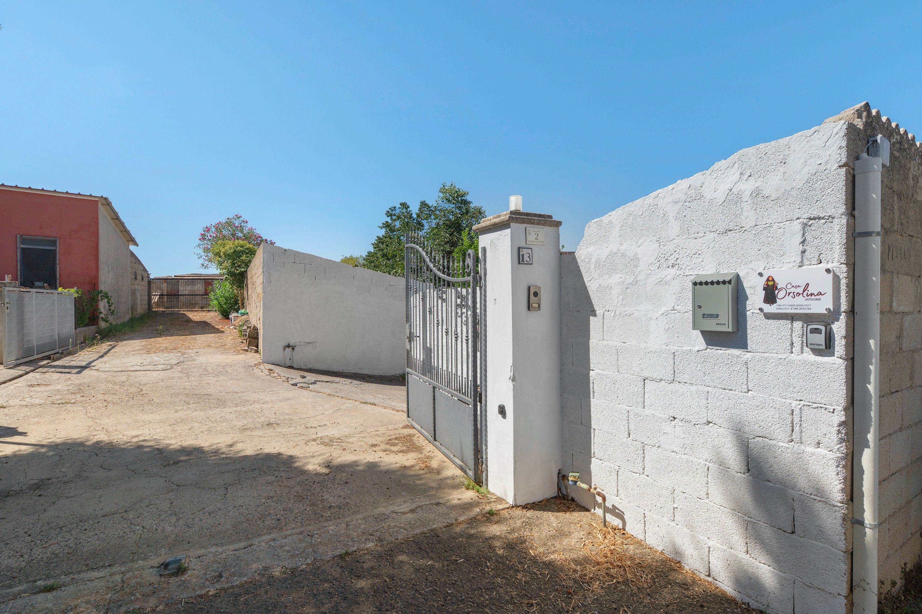 A gated property with a concrete wall, a metal gate, and a building with a red facade in the background.