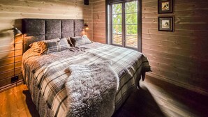 Ein Schlafzimmer in einer Holzhütte mit einem Bett, einem Fenster und zwei gerahmten Bildern an der Wand.