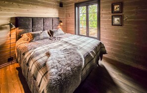 Ein Schlafzimmer in einer Holzhütte mit einem Bett, einem Fenster und zwei gerahmten Bildern an der Wand.