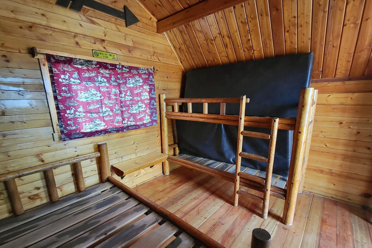 A wooden cabin interior with a bunk bed, a check-out time sign, and a patterned curtain.