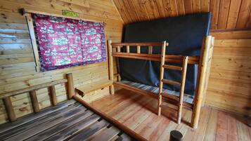 L’intérieur d’un chalet en bois, avec un lit superposé, un panneau indiquant l’heure de départ et un rideau à motifs.