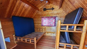 A small, wooden cabin with a loft bed, a bench, and a window with a patterned curtain. - Cheyenne RV Resort (Cheyenne)