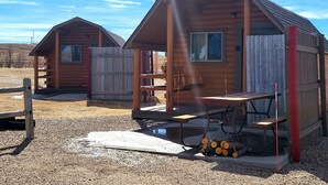 Two wooden cabins with a porch, a window, and a small table. - Cheyenne RV Resort (Cheyenne)
