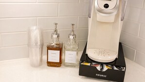 Eine Kaffeemaschine von Keurig mit Wasserbehälter, einem Einwegbecher und zwei Gewürzflaschen auf einer Arbeitsplatte.