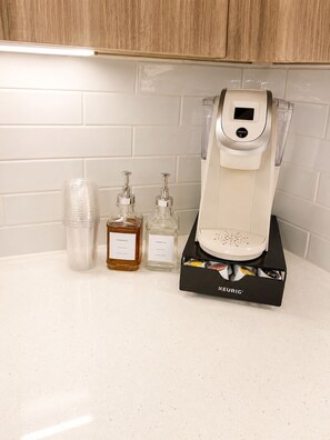A Keurig coffee maker with a water reservoir, a disposable cup, and two condiment bottles on a countertop. - Riverwalk Oasis (San Antonio)