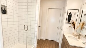 Ein modernes Badezimmer mit Duschkabine aus Glas, weißen Fliesen, Holzboden, Toilette in Weiß und einem Waschtisch mit Spiegel und Dekoration.