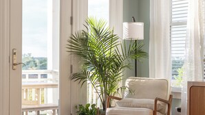 A room with a wooden table, a white chair, a potted plant, and a lamp. - Sunsets, Salty Air, and Waterfront Views (Surf City)