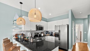 A modern kitchen with white cabinets, a black countertop, and stainless steel appliances. - Sunsets, Salty Air, and Waterfront Views (Surf City)
