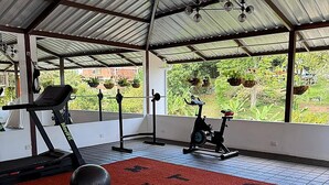 Un gimnasio techado con equipo de ejercicio, una colchoneta roja con la palabra 'California' escrita y vistas al exterior con vegetación.