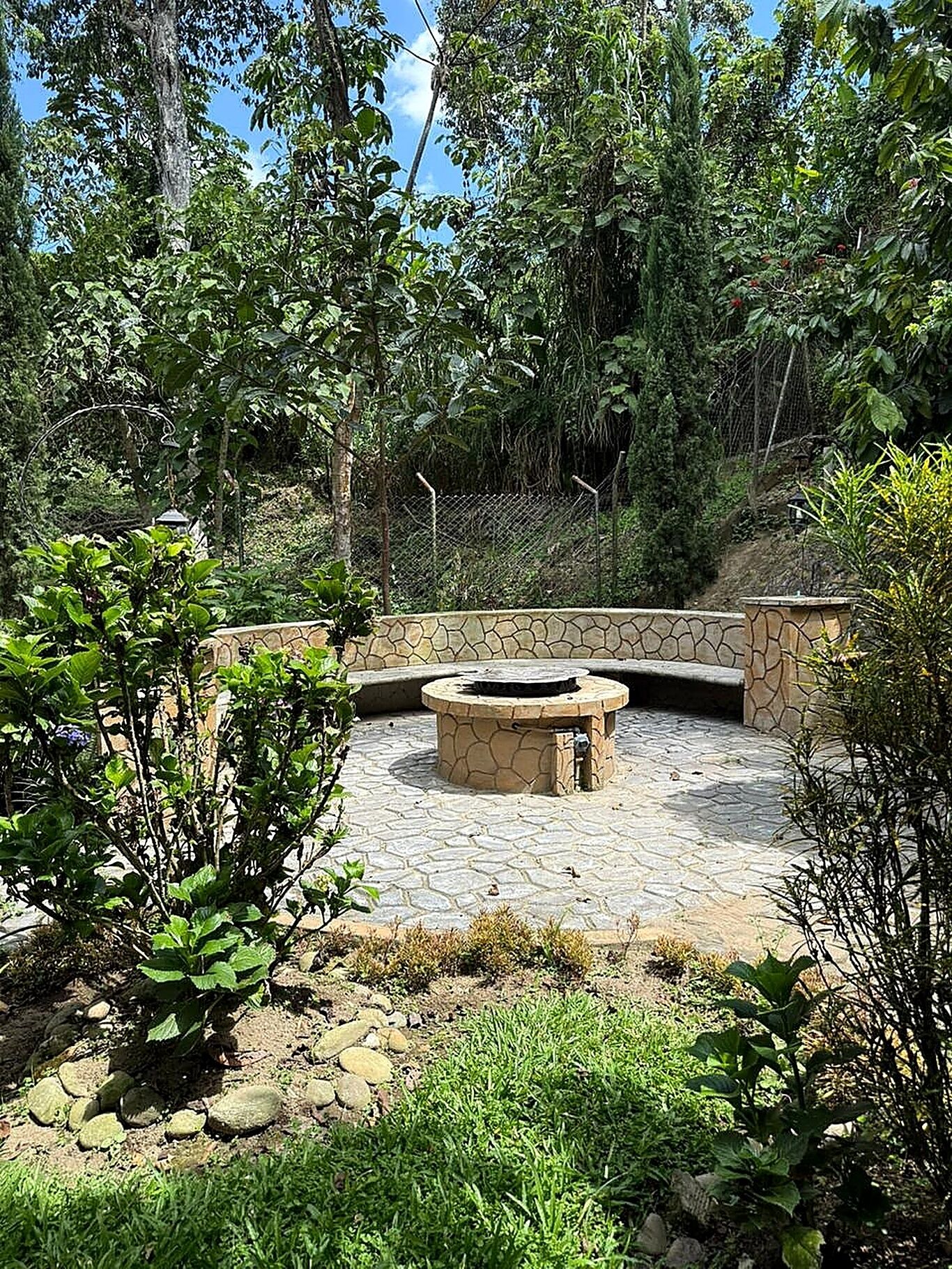 A stone fire pit surrounded by a stone wall, with a grassy area and trees in the background.