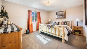 A bedroom with a bed, a dresser, a window with curtains, a bedside table with a lamp, and a framed picture on the wall.