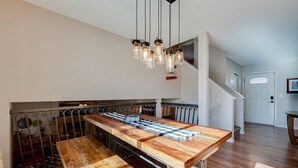 A kitchen with a long wooden table, hanging pendant lights, and a staircase leading to another level.