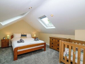 A bedroom with a sloped ceiling, a skylight, a bed, a nightstand, a dresser, and a crib. - 5 Ger Afon (Pwllheli)