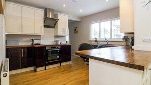 A modern kitchen with white cabinets, a built-in oven, and a wooden countertop. - 5 Ger Afon (Pwllheli)