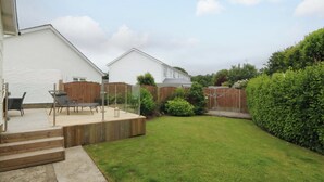 A residential backyard with a wooden deck, a seating area with chairs, and a well-maintained lawn. - 5 Ger Afon (Pwllheli)
