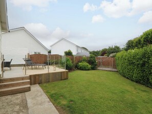 Ein Wohnhausgarten mit einer Holzterrasse, einer Sitzecke mit Stühlen und einem gepflegten Rasen.