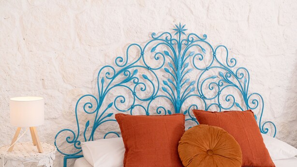 Un lit avec une tête de lit en métal décorative, une literie blanche et deux oreillers marron.
