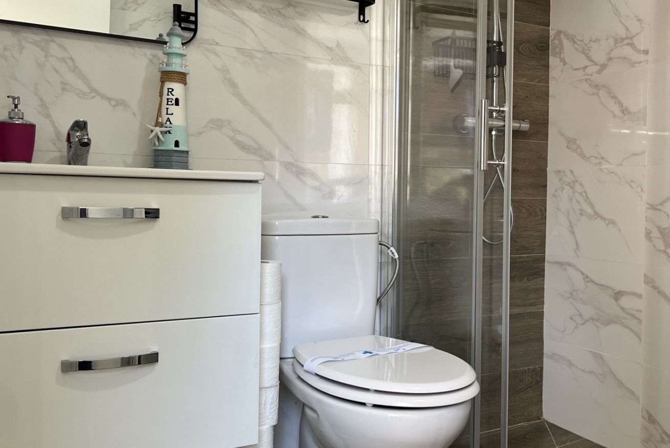 A bathroom with a toilet, a shower enclosure, a marble wall, and a shelf with a lighthouse decoration.
