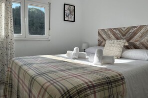 A neatly made bed with a plaid bedspread, a headboard with a geometric pattern, a window with a view of trees, and a framed picture on the wall. - Casa Gatu 307A by R2R (Cudillero)
