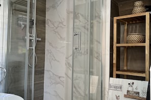A bathroom with a glass shower enclosure, a marble wall, and a wooden shelf with baskets.