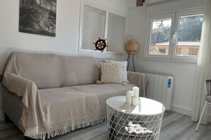 A room with a sofa, a round table with candles, a ship's wheel decoration, and a view of buildings through a window. - Casa Gatu 307A by R2R (Cudillero)