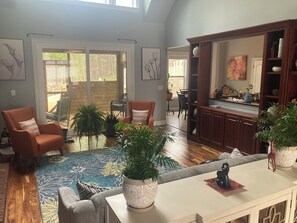Een ruime woonkamer met een bank, stoelen, een salontafel en potplanten.