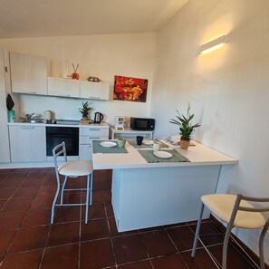 A compact kitchen with white cabinets, a dining area with two chairs, a small island, and a microwave. - A delightful section of a villa surrounded by greenery and just a stone's throw from the sea (Quartu Sant'Elena)