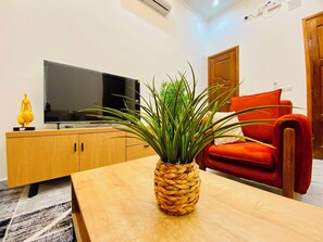 A living room with a television, a wooden cabinet, a woven plant pot, and a red chair.