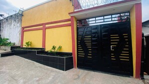 A building with a yellow facade, a black gate with yellow accents, and a security fence topped with barbed wire. - Furnished 1-bedroom apartment with a living room, fully equipped kitchen, and Wi-Fi (Brazzaville)