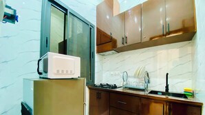 A compact kitchen with a microwave on a small fridge, a gas stove, and a dish rack. - Furnished 1-bedroom apartment with a living room, fully equipped kitchen, and Wi-Fi (Brazzaville)