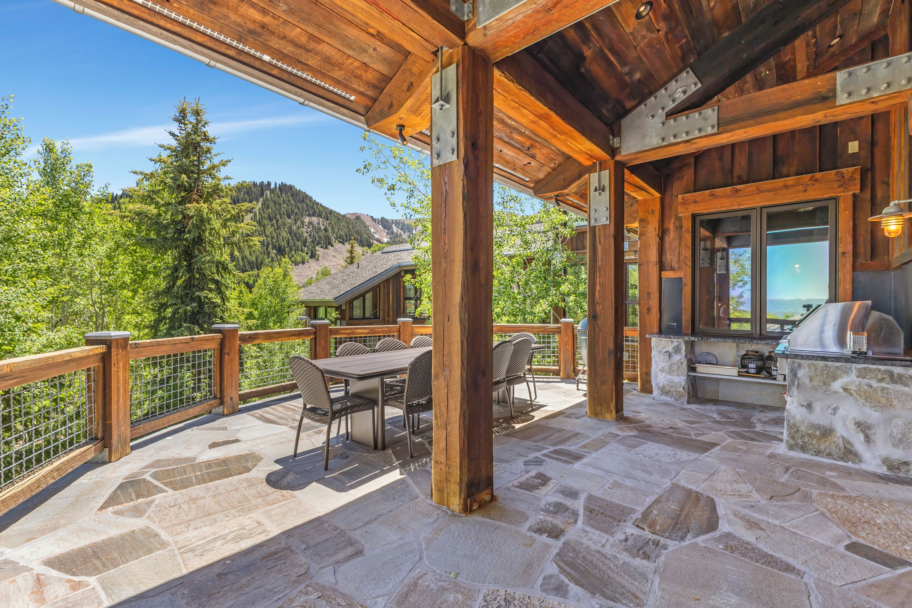 Un patio techado con piso de piedra, mobiliario de madera y vistas a un paisaje montañoso.