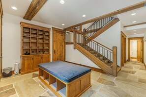 Um quarto amplo com piso de pedra, um banco de madeira, um armário de madeira grande com cestos e uma escada com corrimão de madeira.