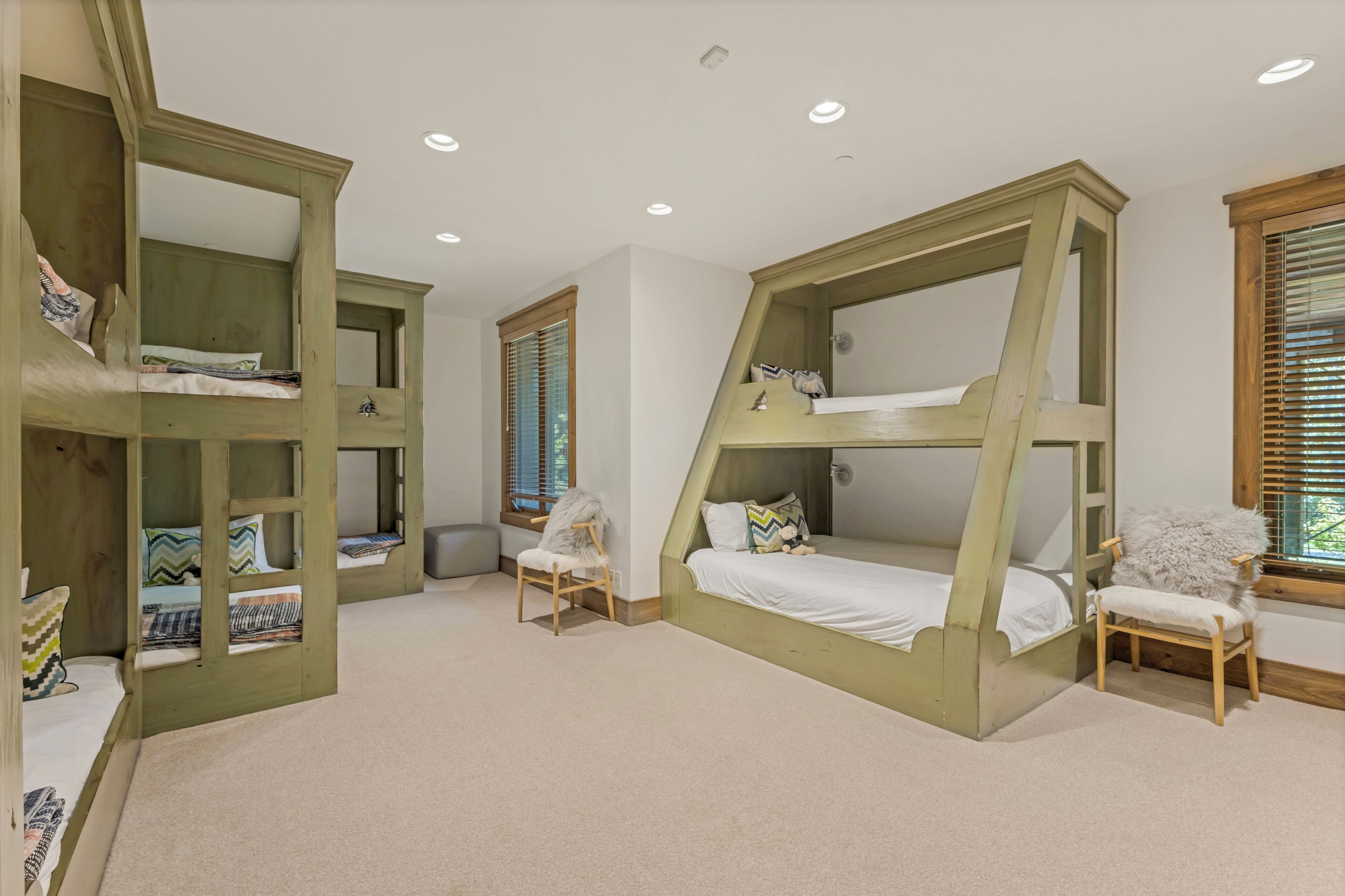 Une chambre avec des lits superposés, une chaise et une fenêtre avec des stores.