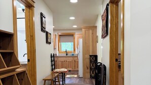 Un pasillo con suelo de madera, una mesa de comedor con sillas, una zona de cocina con armarios de madera y una alfombra estampada.